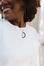 Load image into Gallery viewer, Woman wearing a necklace with a black and silver pendant for sale by Mend on the Move against a blurred background