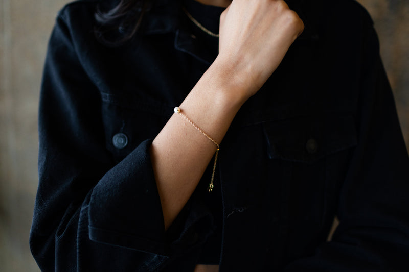 one white freshwater pearl linked to gold plated chain bracelet on arm dark background