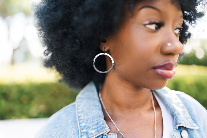 Woman outdoors with an afro wearing a denim jacket with silver and black hoops for sale by Mend on the Move