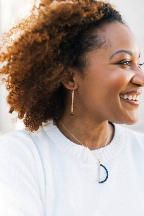 Woman with curly hair wearing a white sweater with a blue logo with copper and glass dangle earrings for sale by Mend on the Move