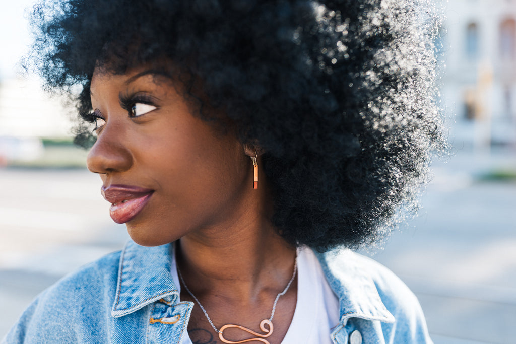 Woman with an afro wearing a denim jacket outdoors with copper earrings for sale from Mend on the Move