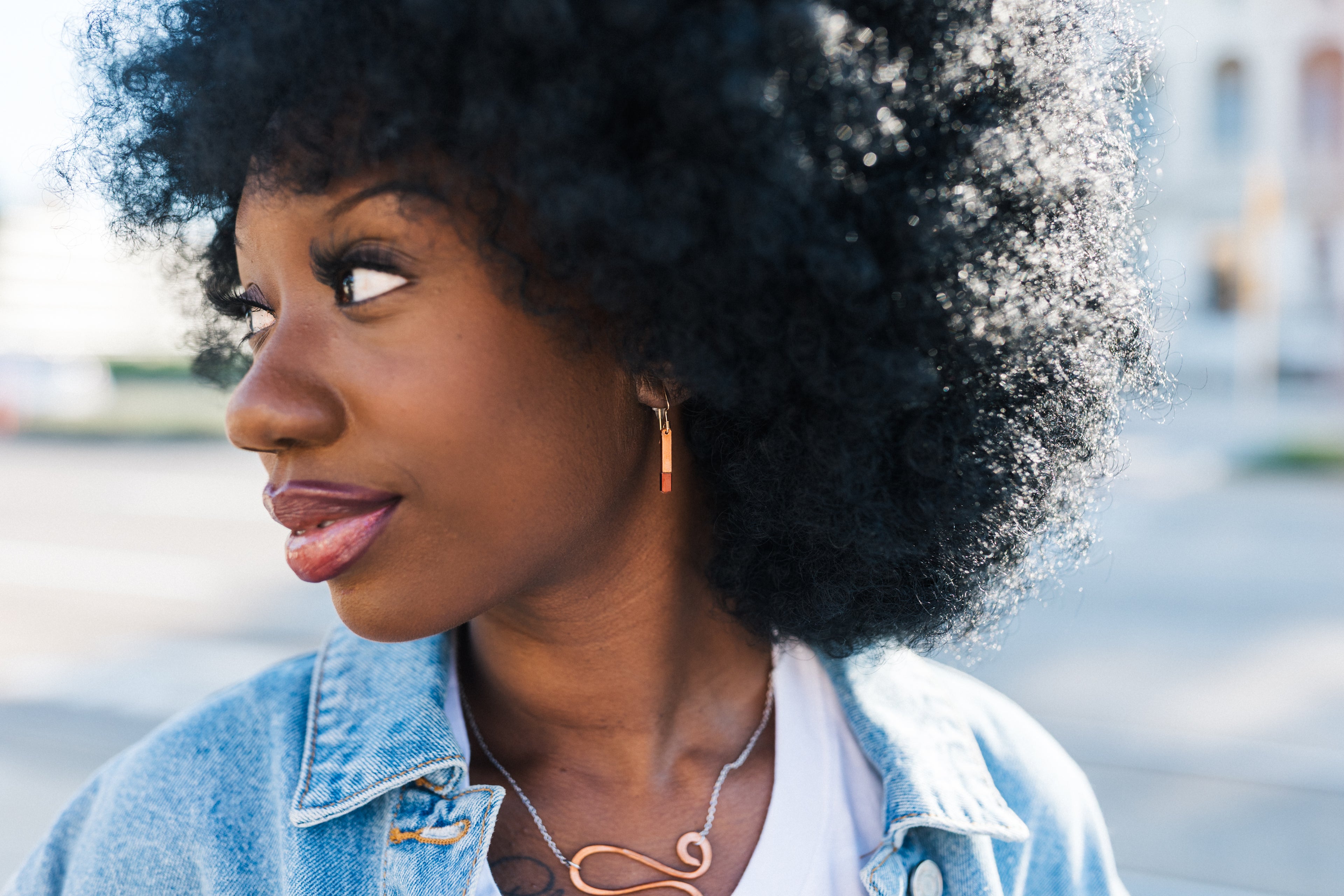 Woman with an afro wearing a denim jacket outdoors with copper earrings for sale from Mend on the Move