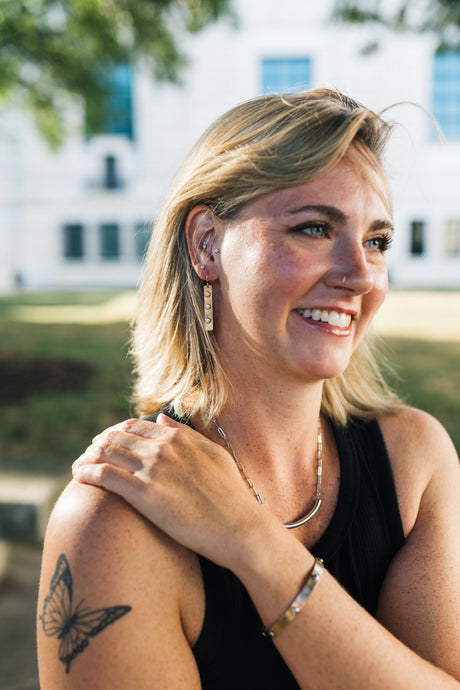 Woman with a butterfly tattoo on her arm, smiling outdoors, wearing copper earrings with steel rivets for sale by Mend on the Move