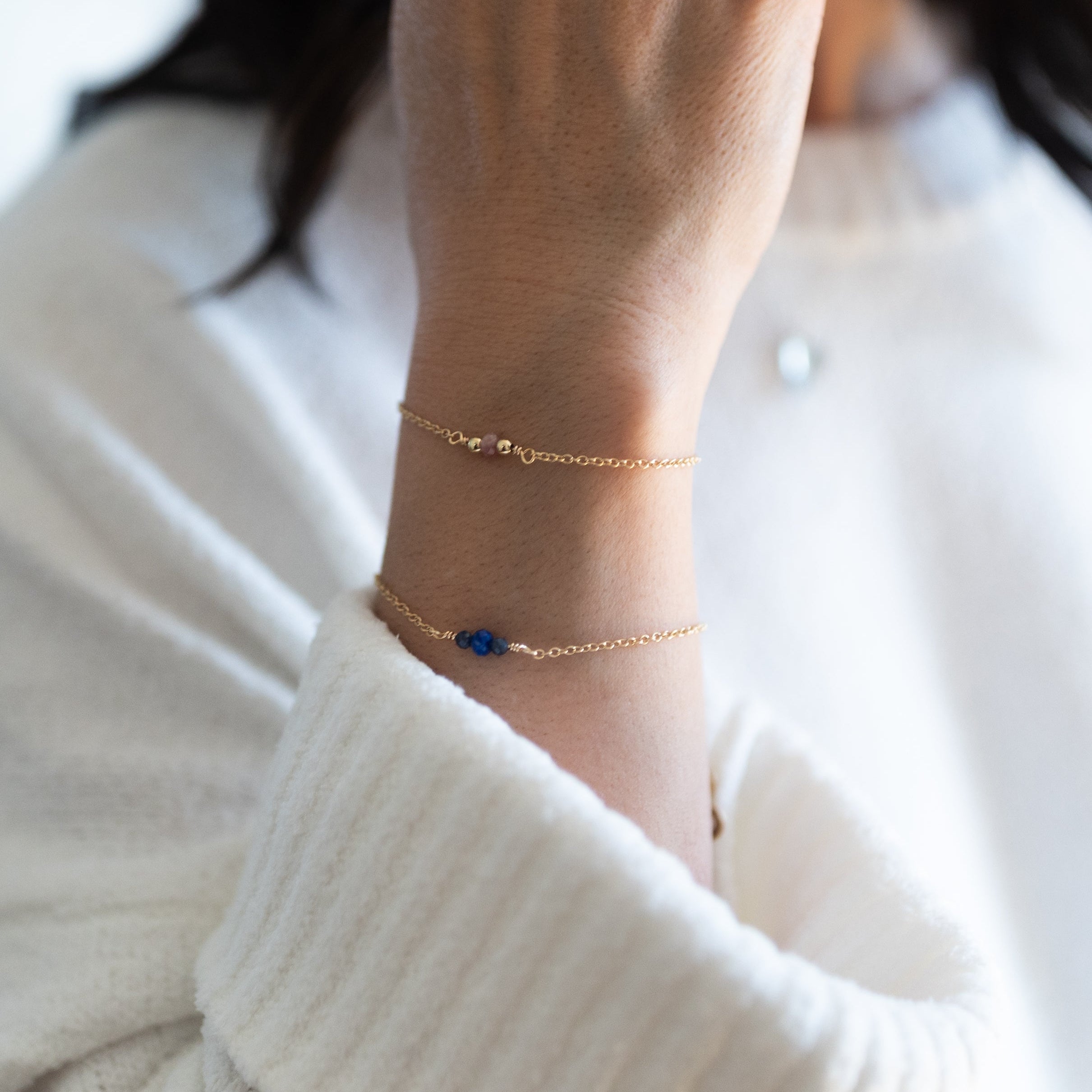 A person wearing a white sweater showcases a gold-plated bracelet with a pink tourmaline bead and a silicone slider bead closure.