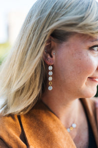 Close-up of a woman wearing silver and gold dangling earrings for sale by Mend on the Move 