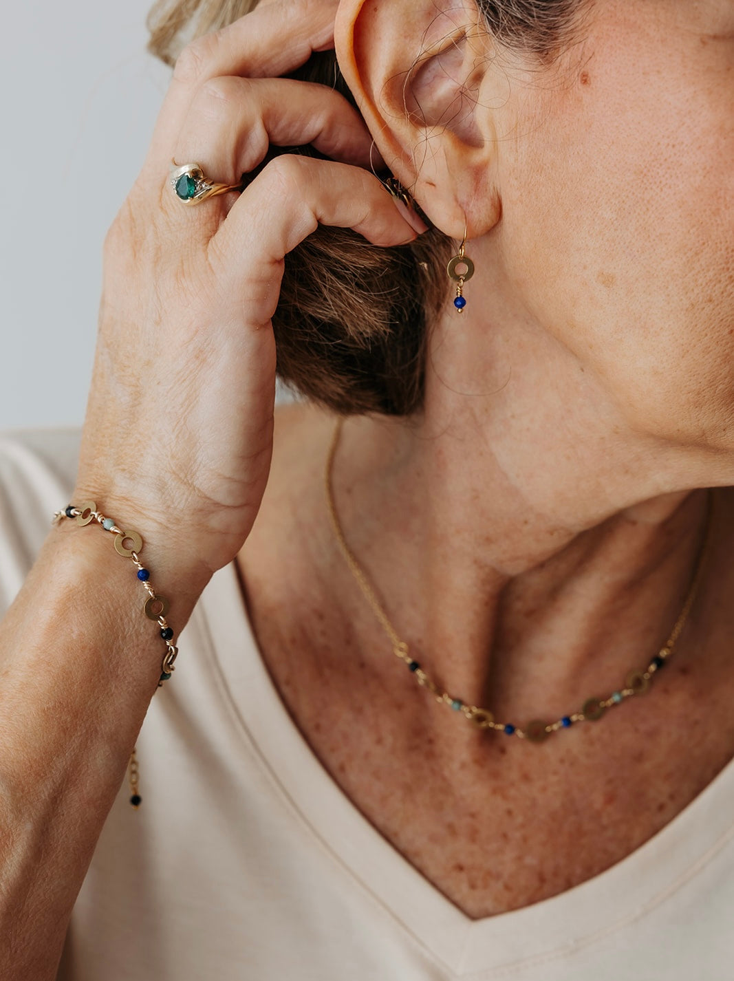 Close-up of a person wearing gold and gemstone jewelry including earrings, a necklace, and a bracelet.