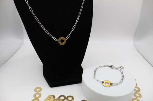 Silver and gold chain necklace on a black bust and bracelet on a white stand with gold circular charms.