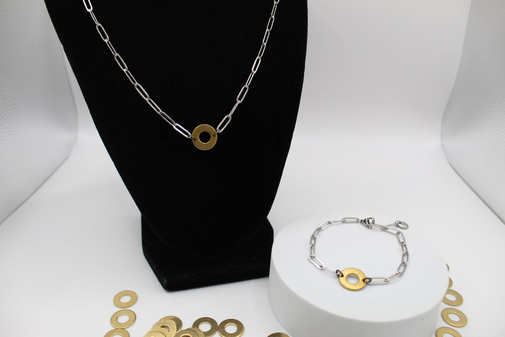 Silver and gold chain necklace on a black bust and bracelet on a white stand with gold circular charms.