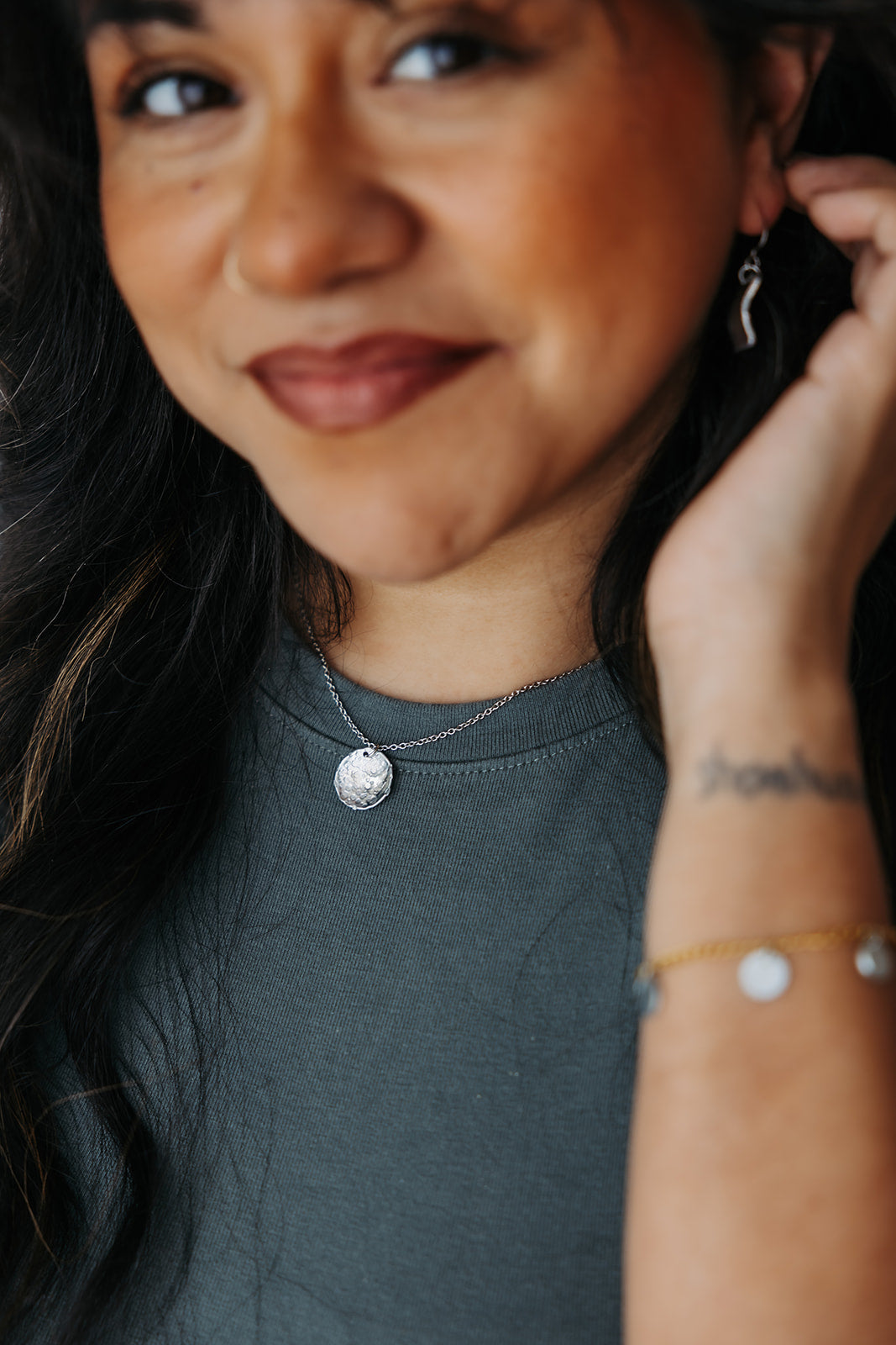 Close-up of a person wearing a necklace and earrings, with a blurred background.