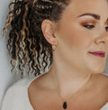 Woman wearing a necklace with a black earring against a neutral background