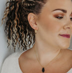 Woman wearing a necklace with a black earring against a neutral background
