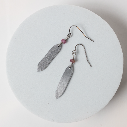 Silver feather-shaped earrings with pink beads on a white round surface