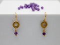 Gold earrings with purple beads on a white surface
