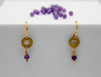 Gold earrings with purple beads on a white surface
