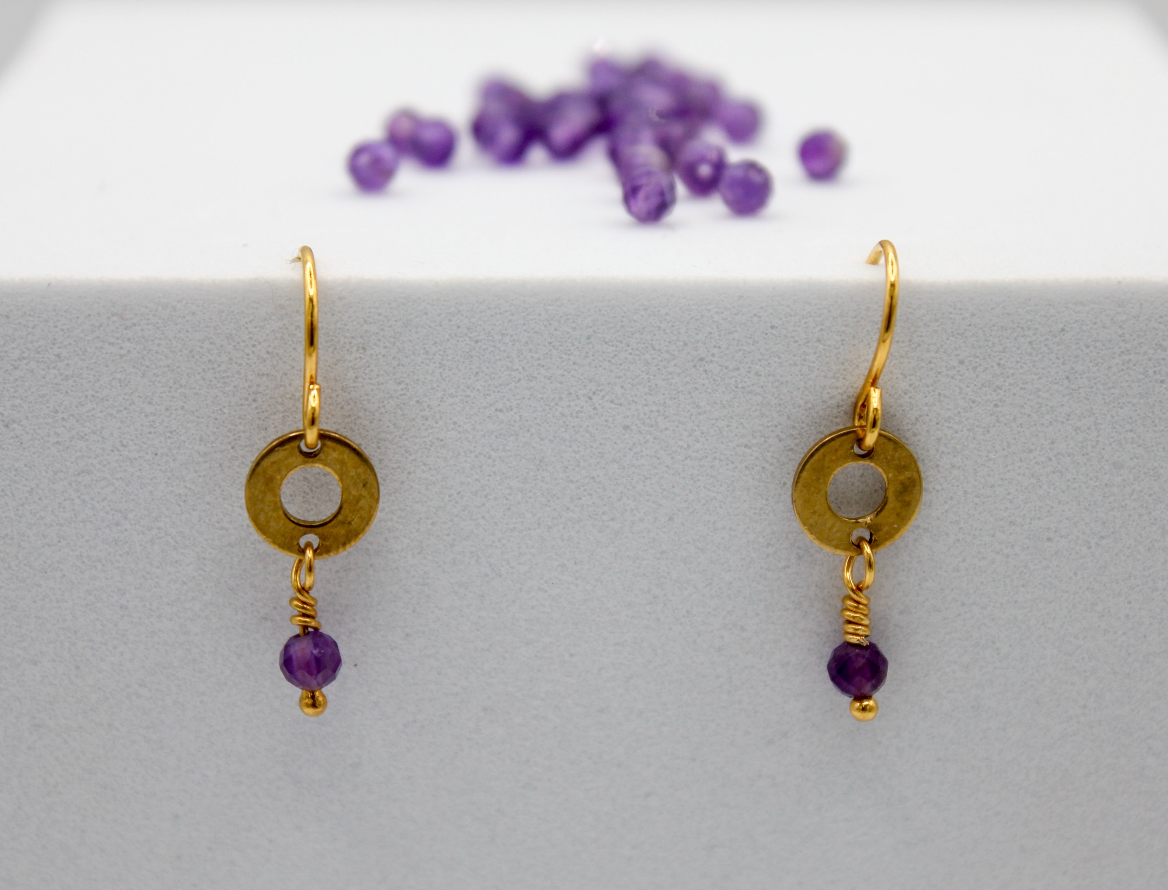 Gold earrings with purple beads on a white surface