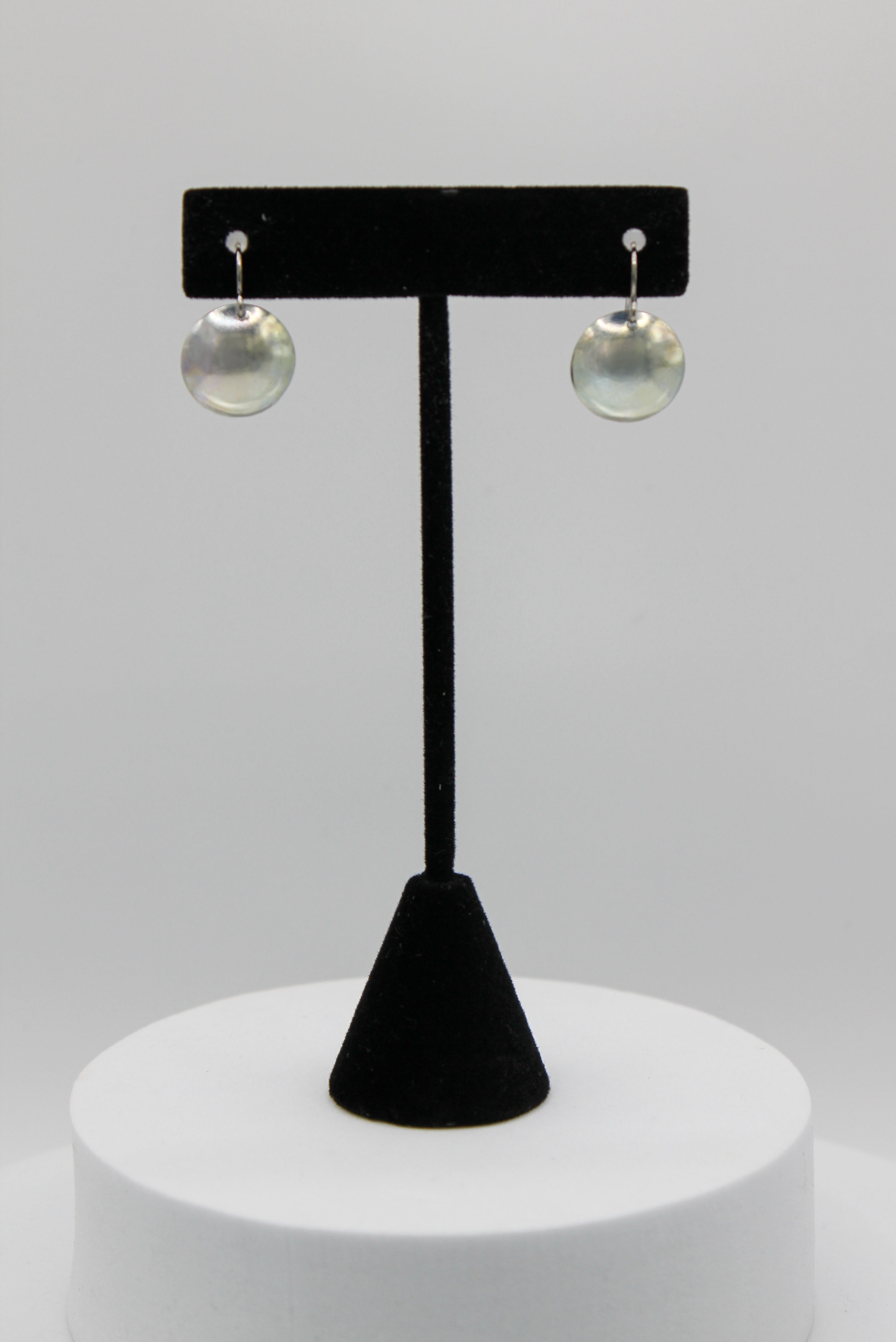 Pair of silver earrings on a black earring stand against a white background