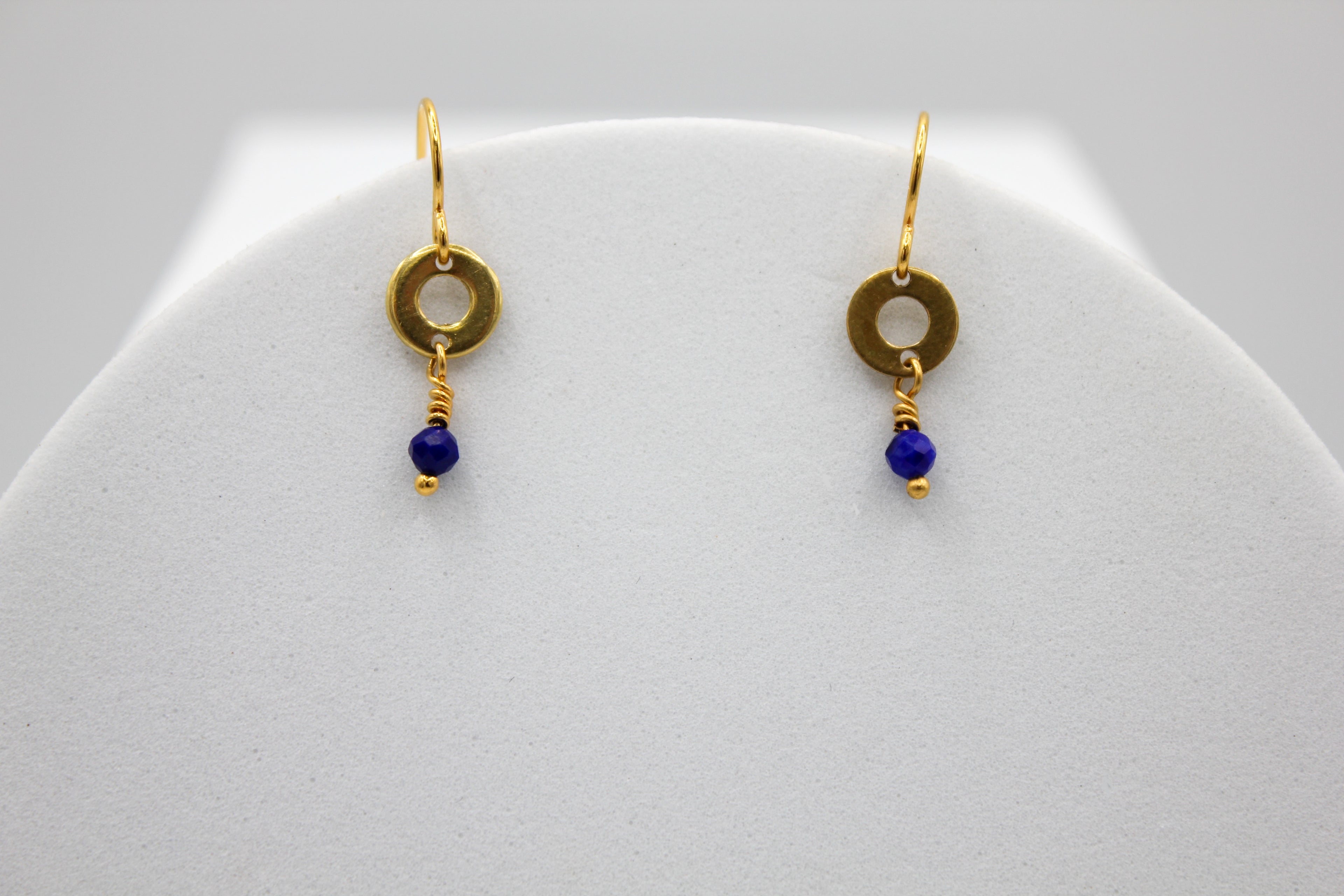 Gold earrings with lapis blue beads on a white stand