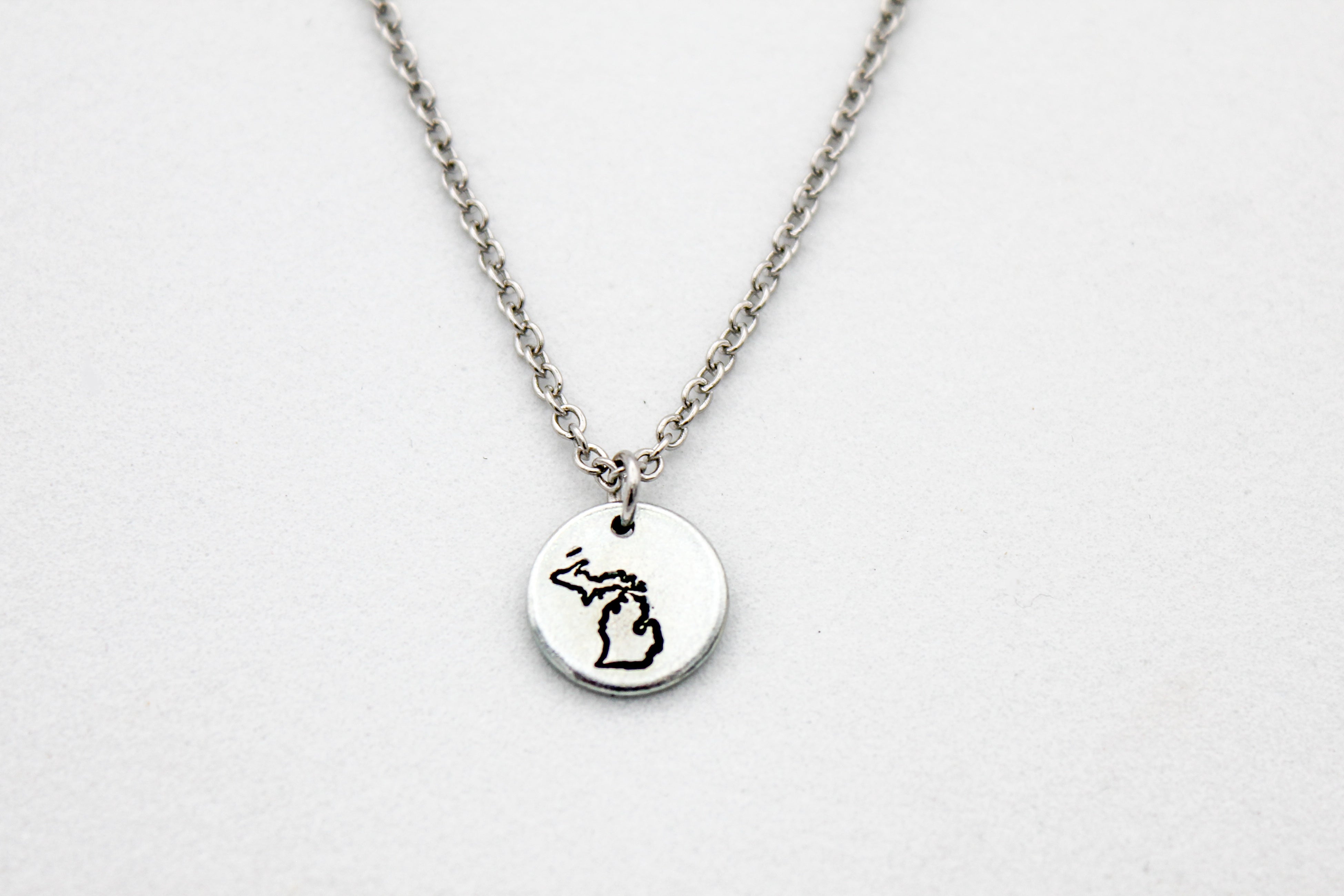 Silver necklace with a round pendant stamped with Michigan Upper & Lower Peninsula on a white background
