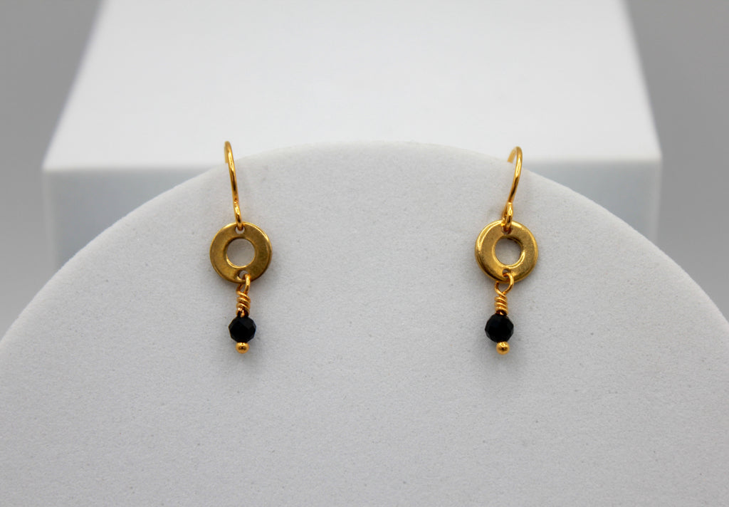 Gold earrings with black beads on a white stand