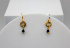Gold earrings with black beads on a white stand