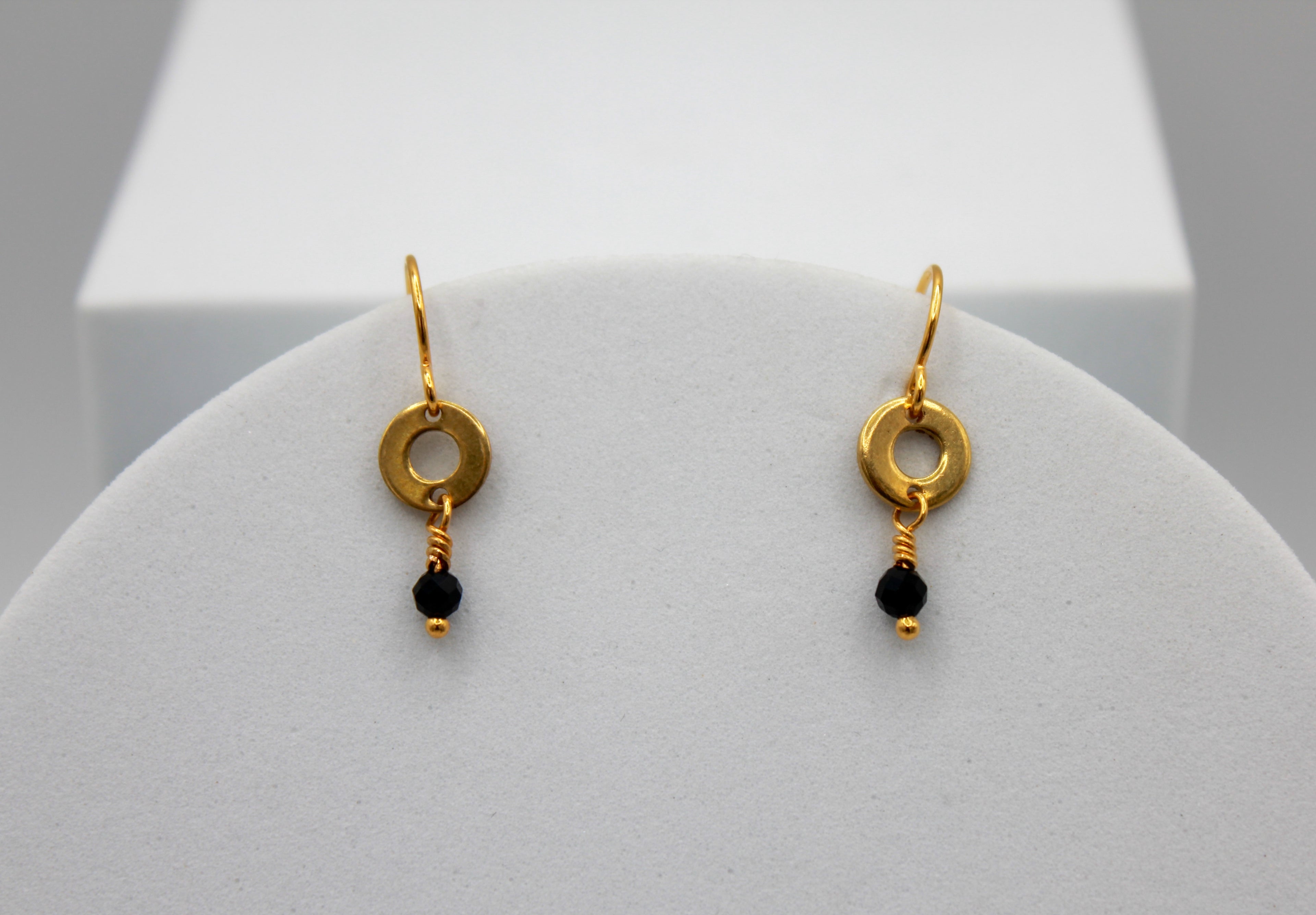 Gold earrings with black beads on a white stand