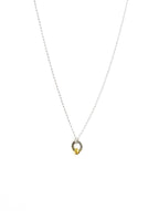 A sterling silver necklace with a small silver charm and gold bead shaped like a seed, on a white background.