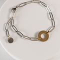 Silver chain bracelet with gold circular charm on a white plate